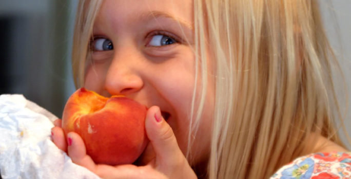 Barn som är allergisk mot kärnfrukt äter en persika.